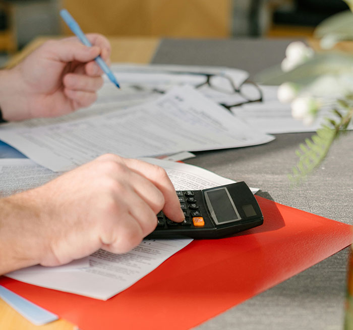 Hands using a calculator on documents, illustrating common scams and financial caution in America.