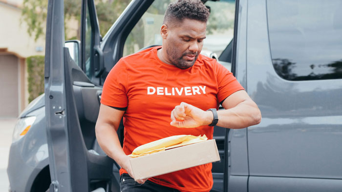 Delivery driver in front of a black van holding a package, checking watch.