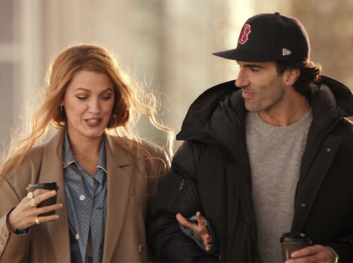 Two people walking with coffee cups, engaged in conversation.