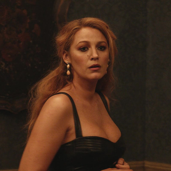 Blake Lively in a low-cut black dress, standing in a dimly lit room from It Ends With Us. Blake Lively in a low-cut black dress, standing in a dimly lit room from It Ends With Us.