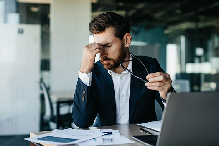 Stressed boss in office holding glasses, realizing mistake after prank firing of key employee.