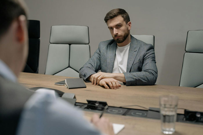 Employee in a meeting room, looking dissatisfied, sitting across from a colleague, highlighting workplace mistreatment. Employee in a meeting room, looking dissatisfied, sitting across from a colleague, highlighting workplace mistreatment.