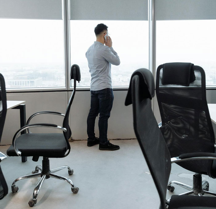 Man standing by office window on phone, four empty chairs, concept of workplace karma. Man standing by office window on phone, four empty chairs, concept of workplace karma.