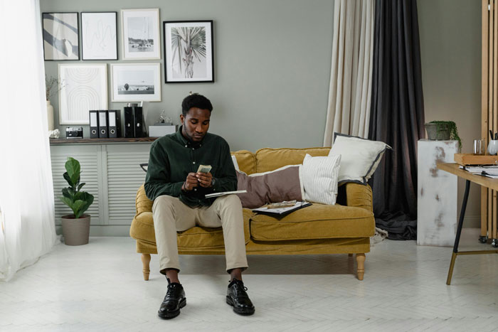 Man looking upset about mortgage payments while sitting on a sofa in a well-decorated living room. Man looking upset about mortgage payments while sitting on a sofa in a well-decorated living room.
