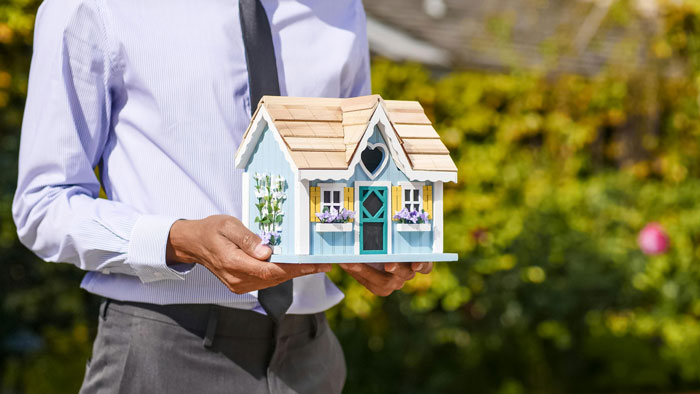 Man in a business shirt holding a small model house, representing mortgage concerns. Man in a business shirt holding a small model house, representing mortgage concerns.