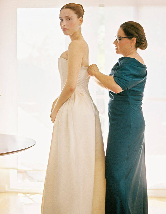 Bride in a dramatic wedding dress, assisted by a woman, showcasing elegance and style. Bride in a dramatic wedding dress, assisted by a woman, showcasing elegance and style.