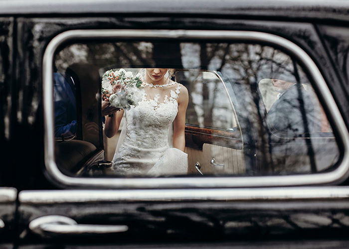Bride in a lace wedding dress holding a bouquet, seen through a car window, symbolizing newlyweds' transportation plans. Bride in a lace wedding dress holding a bouquet, seen through a car window, symbolizing newlyweds' transportation plans.