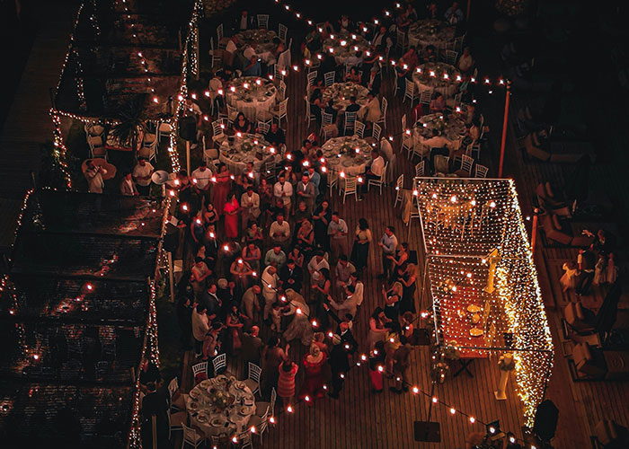 Aerial view of a wedding reception with guests dining and dancing under string lights. Aerial view of a wedding reception with guests dining and dancing under string lights.
