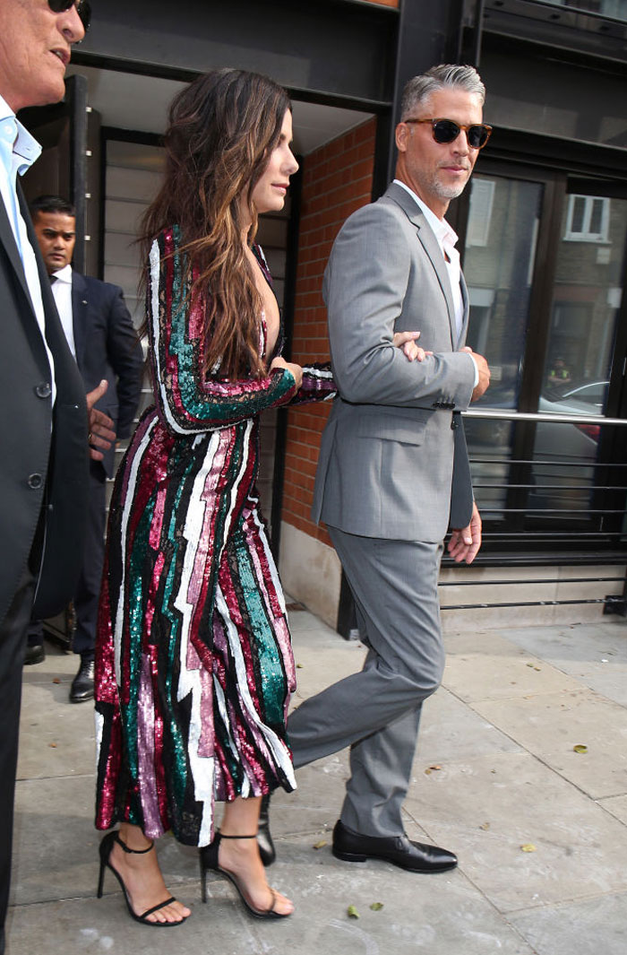 Sandra Bullock in a sequined dress alongside Bryan Randall in a gray suit, outdoors holding arms.