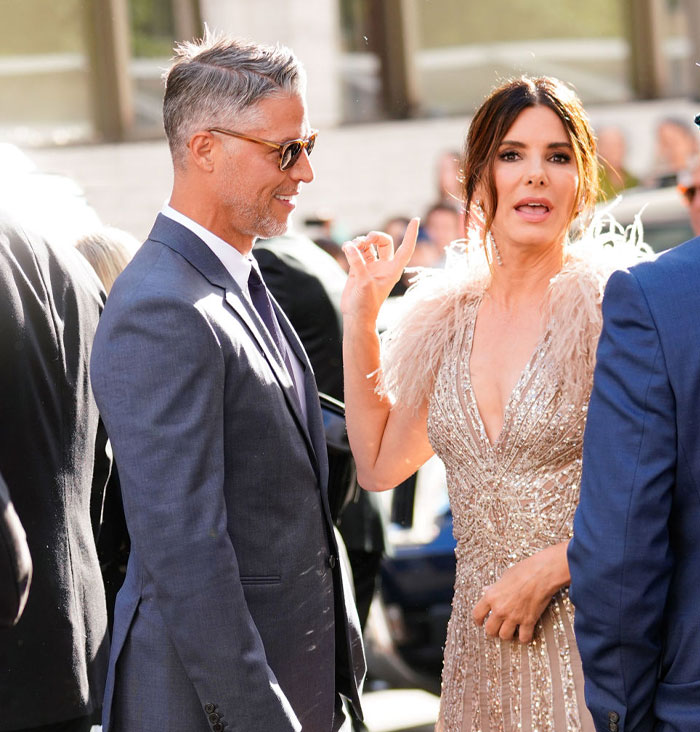 Bryan Randall in a gray suit and Sandra Bullock in an elegant dress at an event, capturing a moment of connection and style.