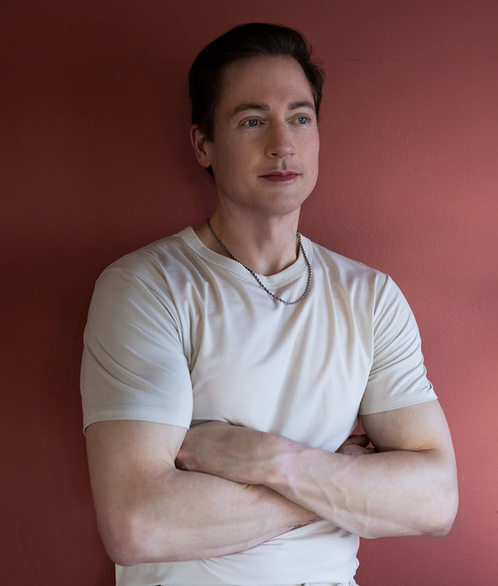 Bryan Johnson in a white shirt standing against a red wall.