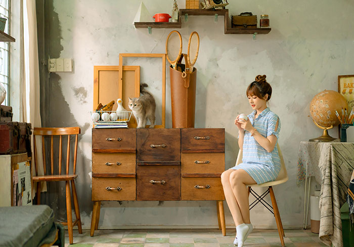 Pet sitter enjoys a drink while a cat sits on a wooden dresser in a vintage-styled room. Pet sitter enjoys a drink while a cat sits on a wooden dresser in a vintage-styled room.