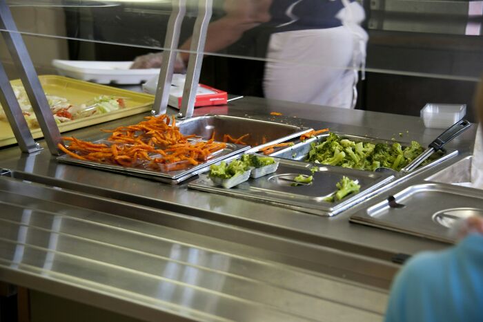 Cafeteria food options include trays of broccoli and carrots, highlighting dietary choices linked to weight gain.
