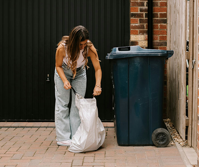 Woman placing garbage in a bin outside, highlighting garbage collection issues. Woman placing garbage in a bin outside, highlighting garbage collection issues.