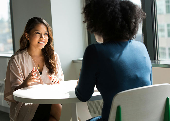 Two women exchanging life cheat codes in a well-lit office setting.