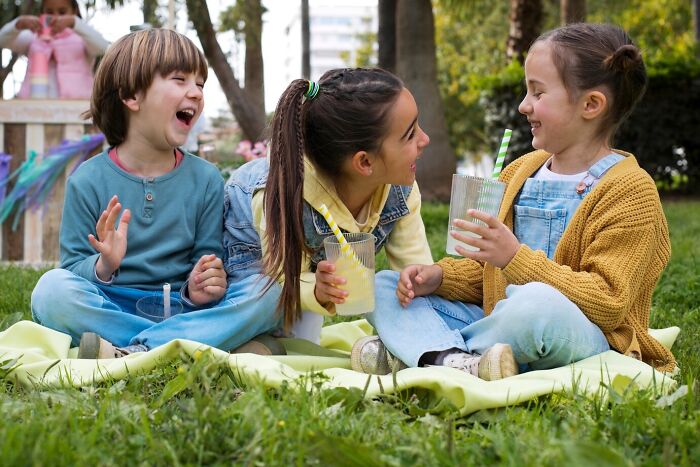Children laughing and chatting while sitting on grass, drinking lemonade, capturing the essence of playful kids at school.