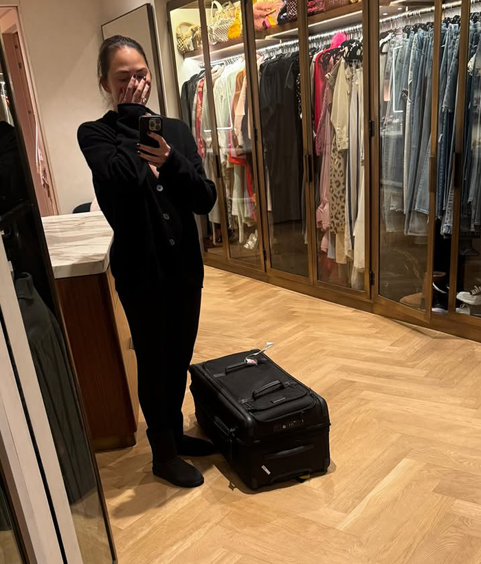 Celebrity in a closet, holding a phone with a suitcase nearby, amidst criticism during LA wildfires. Celebrity in a closet, holding a phone with a suitcase nearby, amidst criticism during LA wildfires.