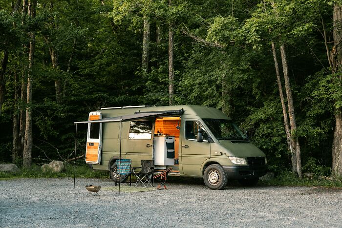 Affordable camper van setup with chairs and a table in a forest setting, illustrating simple living.