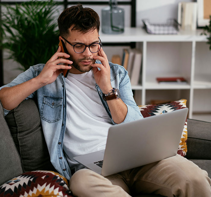 Man on phone and laptop, planning every day revenge due to unpaid client work.