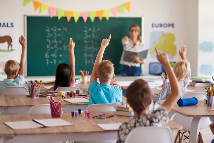 Classroom scene with children raising hands, engaging in a lesson about history facts not taught in school.