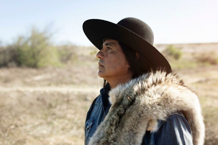Native American man wearing a wide-brimmed hat and fur draped over shoulder, symbolizing untaught facts to complete history.
