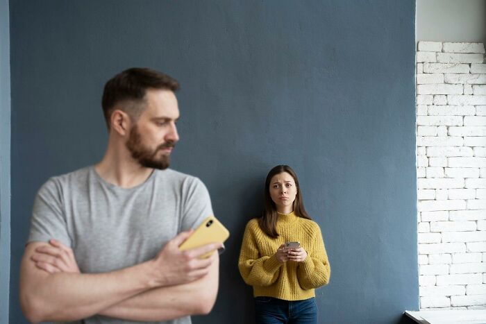 Man with a phone ignoring concerned woman in a yellow sweater, illustrating neighbor communication issue.