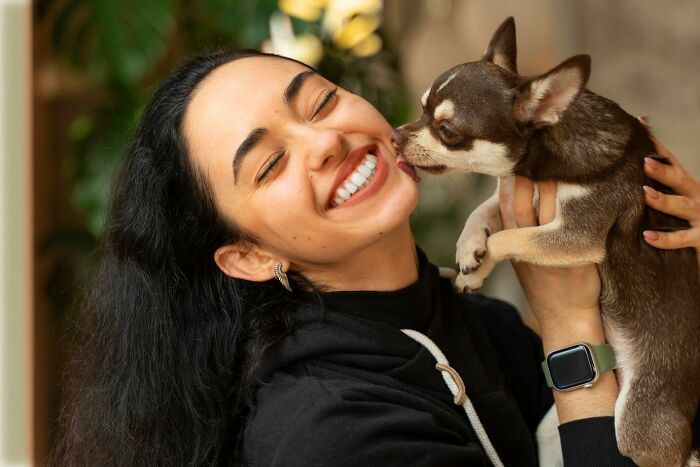 Smiling woman holding a small dog close to her face, wearing a smartwatch.