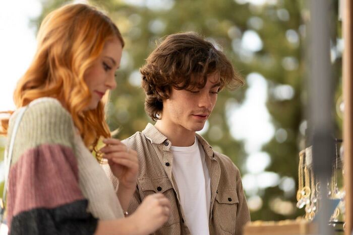 Man and woman standing outdoors, looking at items, with focus on neighbor relations.