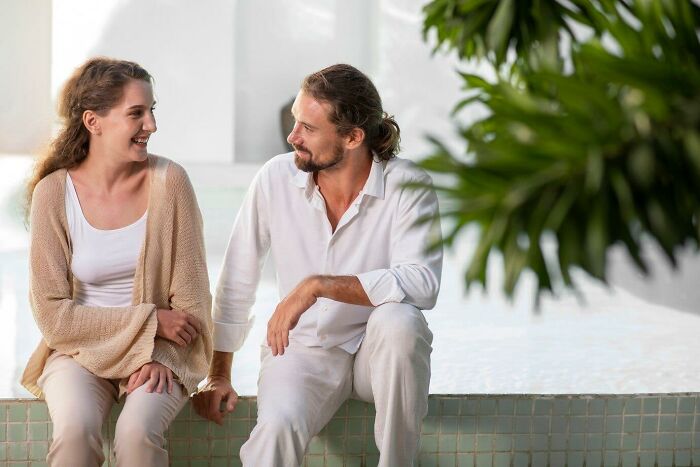 Woman and man sitting by a pool, engaged in conversation regarding a neighbor's behavior.
