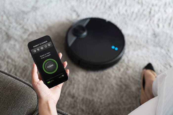 Person using smartphone to control a robot cleaner on a carpet, highlighting trend resistance.
