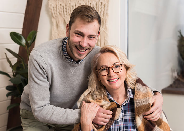 Smiling woman and young man share a warm moment indoors, hinting at family secrets like those in horror movie stories.
