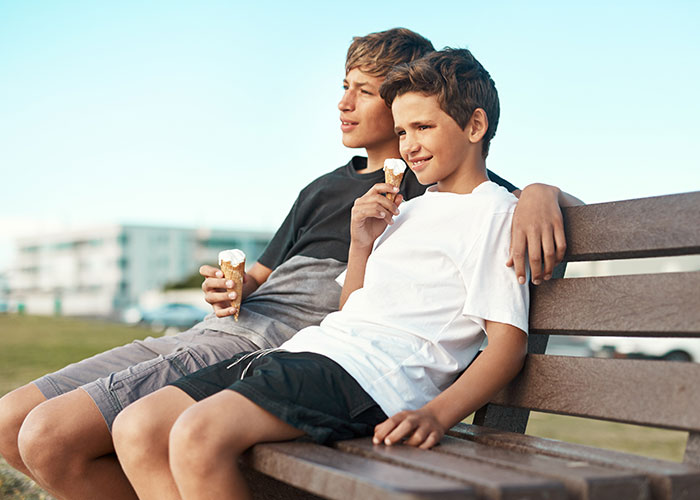 Two boys sitting on a bench enjoying ice cream, evoking themes of family secrets and horror movie-worthy stories.
