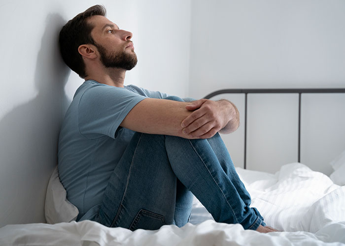Young man sitting on bed looking thoughtful and distressed, reflecting on horror movie-worthy family secrets.