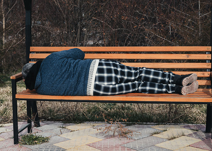 Person lying on a wooden bench outdoors wearing a blue sweater and plaid pants, illustrating family secrets and horror themes.