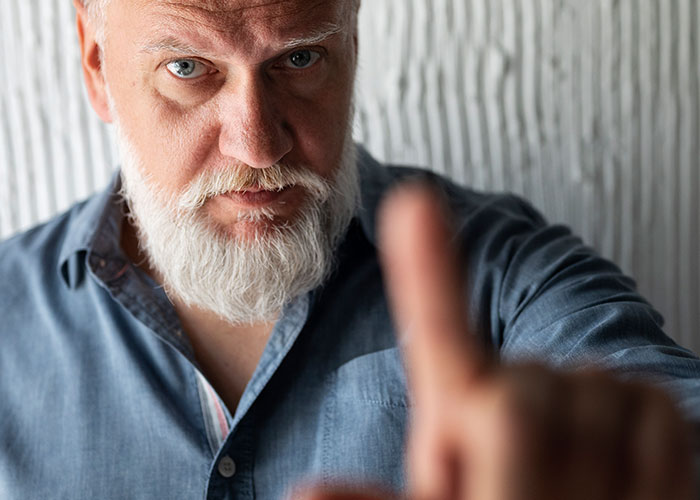 Older man with white beard pointing intensely toward the camera, hinting at horror movie-worthy family secrets.