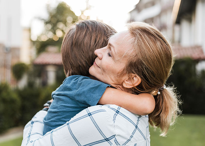 Woman embracing child outdoors, conveying emotional family connection and hints of deep family secrets and horror.