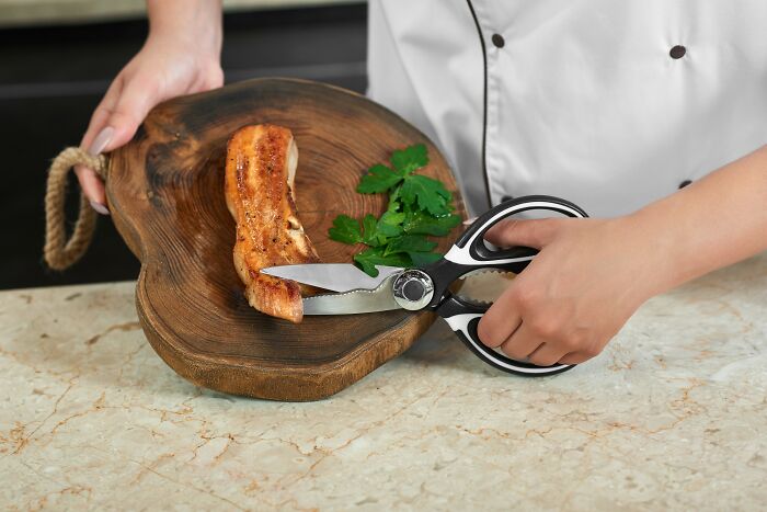 Chef using kitchen shears to cut roasted meat on a wooden board with herbs, showcasing a space-saving purchase.