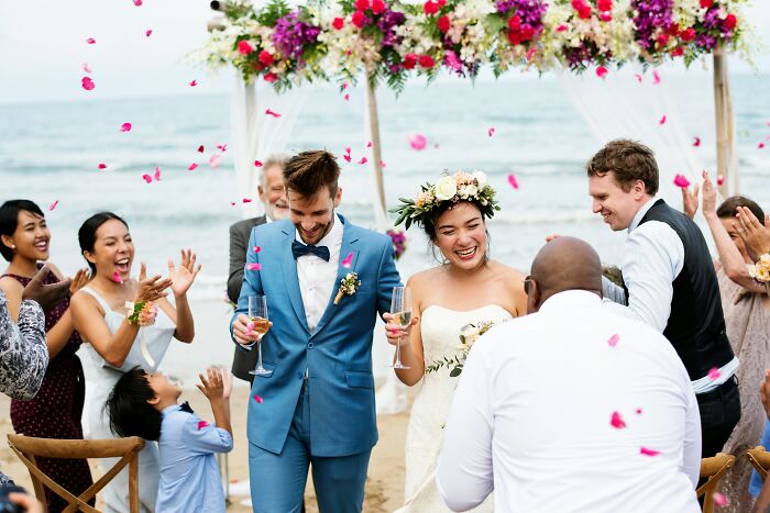 Couple celebrating a wedding on the beach, surrounded by guests, embodying unique personal style over following trends.