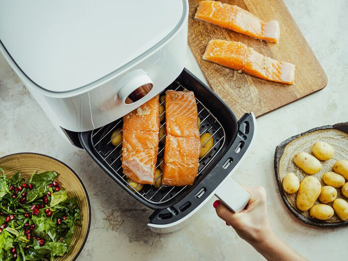 Air fryer with salmon fillets and potatoes, showcasing an affordable way to make life easier.