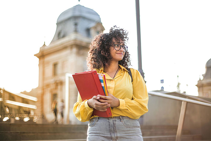 Young woman holding books, contemplating college tuition options outside a historic building. Young woman holding books, contemplating college tuition options outside a historic building.