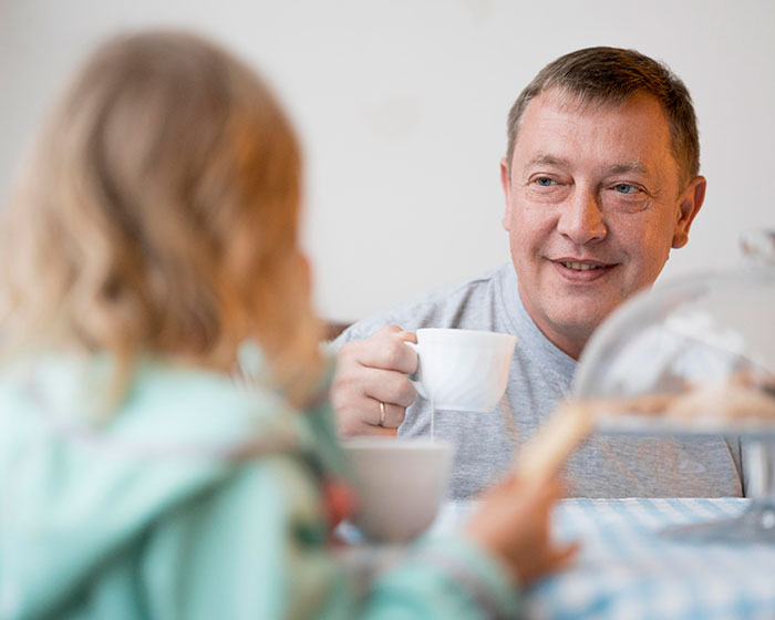 Man smiling at child over coffee, reflecting on granddaughter prioritizing family. Man smiling at child over coffee, reflecting on granddaughter prioritizing family.