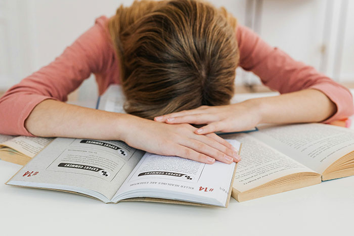 A stressed student resting on open books, related to college tuition and family priorities. A stressed student resting on open books, related to college tuition and family priorities.