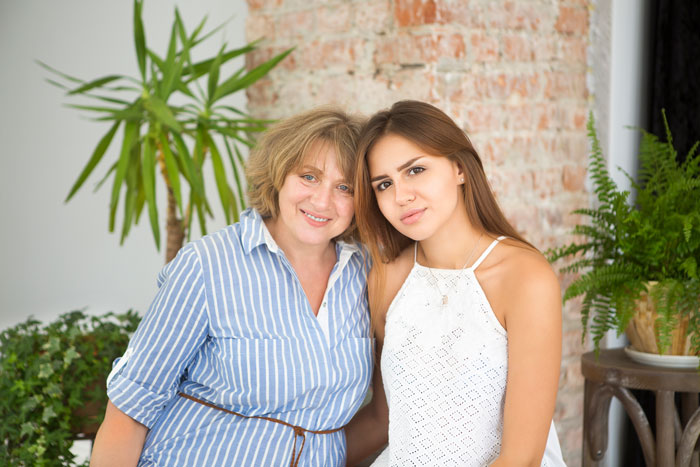 Two women posing together indoors, surrounded by plants, expressing contentment and family bond.