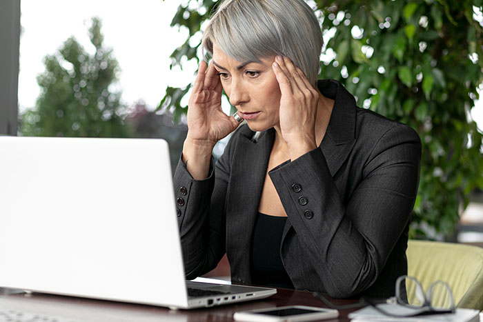 Woman in a suit looking stressed at a laptop, shocked by a hefty bill from a teen's vacation with a friend's family. Woman in a suit looking stressed at a laptop, shocked by a hefty bill from a teen's vacation with a friend's family.