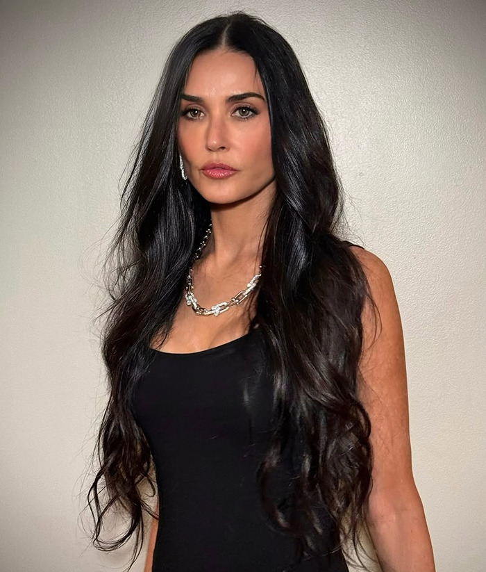 Demi Moore in a black dress posing against a plain background.