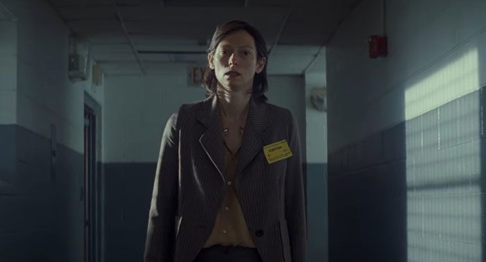 A woman stands alone in a dimly lit hallway, conveying a sad and depressing movie ending.