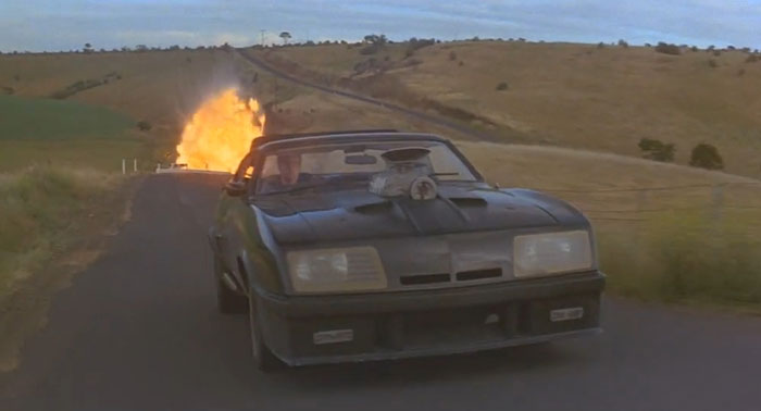 Car driving on a deserted road with an explosion in the background, depicting a sad movie ending.