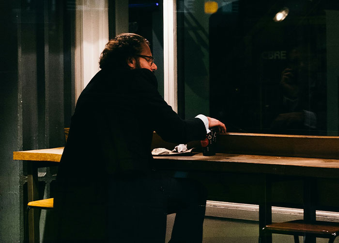 Person waiting alone at a restaurant table at night, looking out the window.