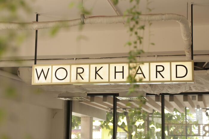 "WORK HARD sign hanging from ceiling, symbolizing outdated financial stereotypes about work ethic."