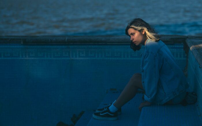 Person sitting thoughtfully by an empty pool, wearing a denim jacket, symbolizing intelligence through introspection.